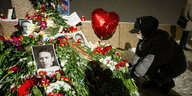 Eine vermummte Frau legt Blumen an einem Gedenkstain ab. Dort liegen viele Fotos von Nawalny und es schwebt ein Luftballon in Form eines roten Herzes