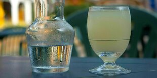 Ein Glas Pastis mit Wasserkaraffe steht auf einem Tisch im Freien