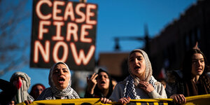 Frauen mit Kopftuch halten ein Schild mit der Aufschrift "Ceasefire now"