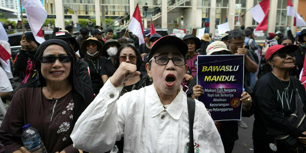 Frauen protestieren in Jakarta gegen angeblichen Wahlbetrug - eine Frau erhebt die Faust - im Hintergrund Flaggen