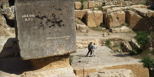 zwei alte Männer spazieren durch eine Steinruine im nahen Osten, links von ihnen ein riesiger Steinquader, bestimmt fünfmal höher als die beiden
