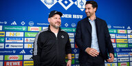 Steffen Baumgart (l) und Jonas Boldt, Sportvorstand des HSV, stehen während der Vorstellung von Baumgart als neuer Cheftrainer des Hamburger SV im Rahmen einer Pressekonferenz nebeneinander. Beide tragen schwarz. Hinte ihnen eine Sponsorenwand
