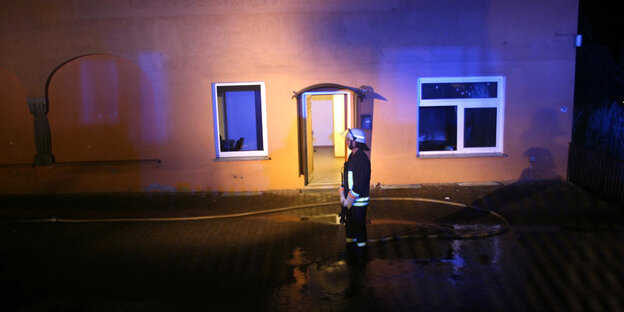 Ein Feuerwehrmann steht in der Nacht vor dem Haus auf welches der Anschlag verübt wurde