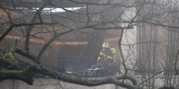 Ein Mitarbeiter der Feuerwehr begutachtet das verkohlte Dach einer Unterkunft