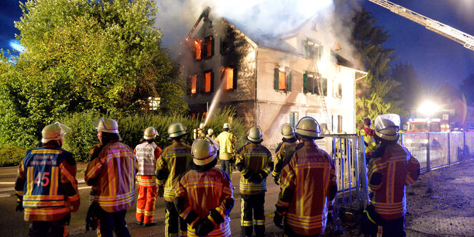 Feuerwehrleute gucken auf das Dach eines Hauses, was gelöscht wird.