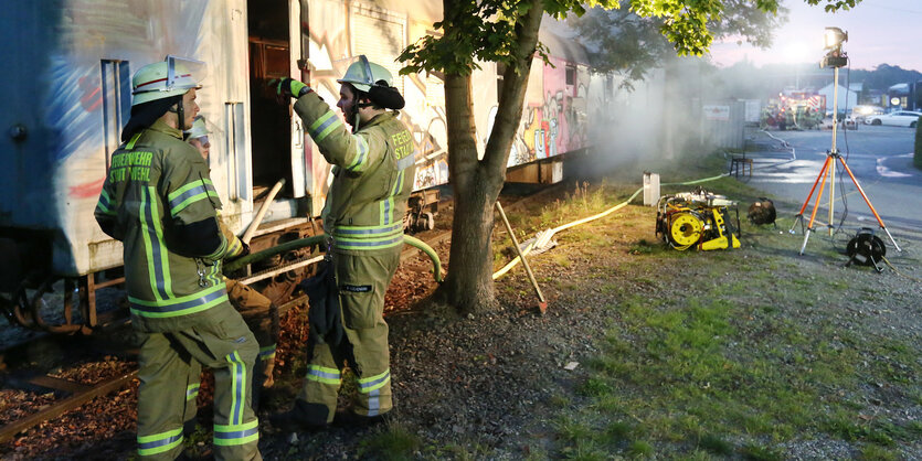 Feuerwehrleute unterhalten sich vor einem ausgebrannten Wagon