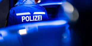 Ein Polizist steht neben einem Polizeiauto - es ist dunkel und das Bild ist bläulich