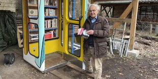 Eine alte Telefonzelle außen bunt bemalt, innen viele Bücher: Konrad Kutt vor der neuen BücherboXX Gleis 17 im Sägewerk Grunewald