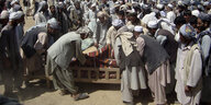 Eine große Gruppe von afghanischen Männern steht um ein Holzgestell, auf dem sie getötete AfghanInnen in Tücher wickeln
