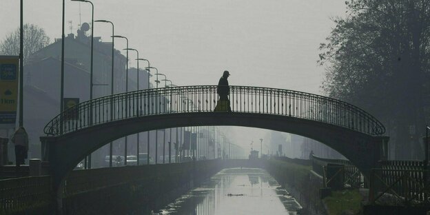 Ein Mann geht über eine Brücke über den Kanal Naviglio Pavese, der in Nebel und Smog gehüllt ist.