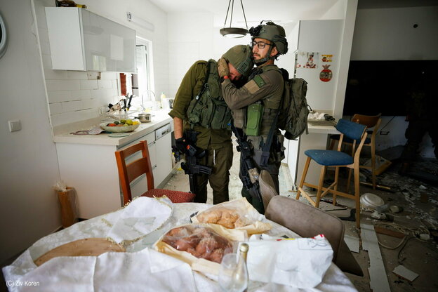 Ein israelischer Soldat wird von seinem Kommandeur tröstend in den Arm genommen. Sie stehen vor einem Tischvor einem Shabbat-Mahl in einer Küche im Kibbuz, der von Terroristen der Hamas am 7. Oktober 2023 zerstört wurde