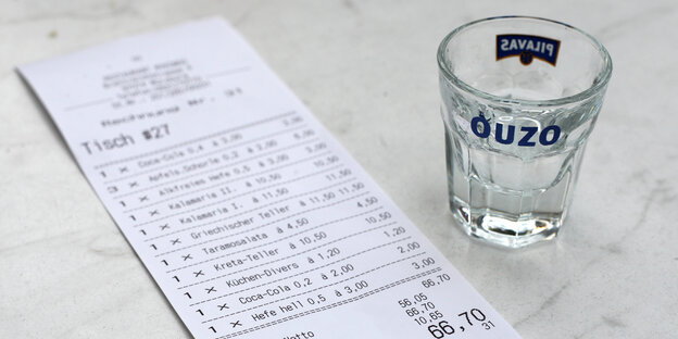 Auf einem Tisch liegt eine Rechnung für Speisen und Getränke neben einem leeren Ouzo-Glas.