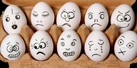 Karton mit weissen Eiern, die mit Gesichtern bemalt sind die einen traurigen, schlecht gelaunten, zornigen Eindruck machen