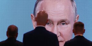 Ein Bild von Putins Kopf auf einer Großleinwand, davor drei Männer
