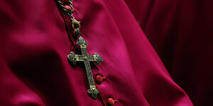 Ein Bischof in roter Kleidung, zu sehen ist nur das Kreuz auf seiner Soutane