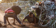 Flüchtlinge kriechen unter einem Stacheldrahtzaun durch