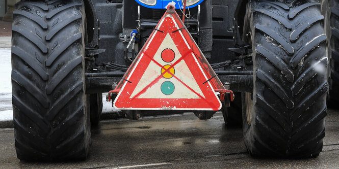 Die großen Reifen eines Treckers, an dem ein Schild mit einem durchgestrichenen Ampelzeichen befestigt ist