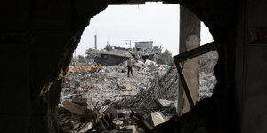 Durch eine Loch in der Wand sieht man einen Trümmerhaufen, auf dem ein Mann steht, in Rafah, Gaza