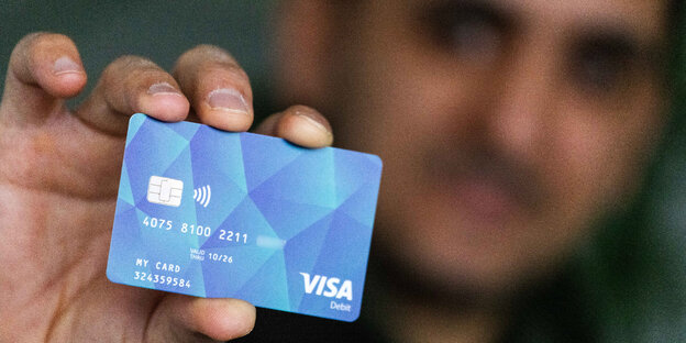 Ein Mann hält eine blaue Plastikkarte mit dem Visa-Logo in die Kamera.