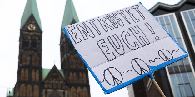 Ein Schild mit der Aufschrift "Entrüstet euch!" wird vor dem Bremer Dom hochgehalten