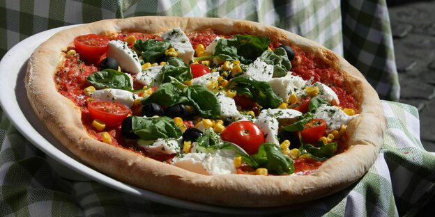 Eine Pizza belegt mit Tomaten, Mozzarella und Basilikumblättern