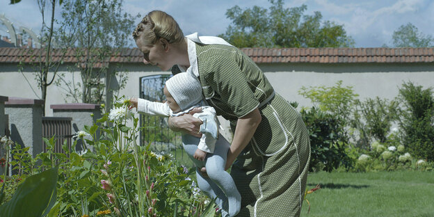 Sandra Hüller steht als Ehefrau des Lagerkommandanten Rudolf Höß in einer Szene im Garten mit dem Baby auf dem Arm und sie betrachten Blumen