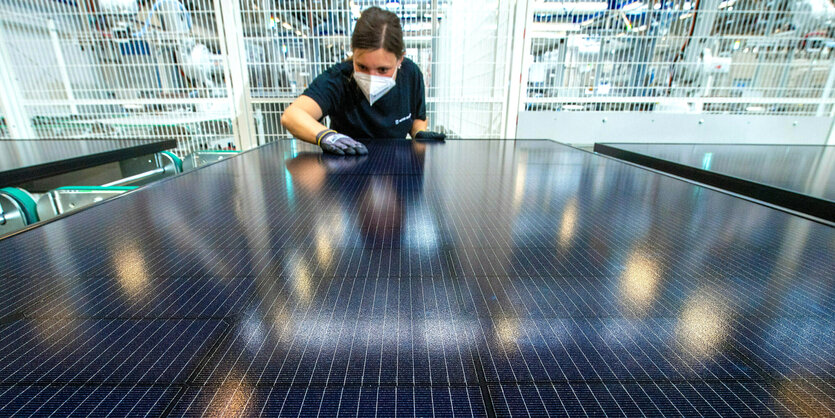 Eine Mitarbeiterin von Solar Burger in Freiberg streicht mt Handschuhen über Solarmodule, sie trägt auch einen Mundschutz