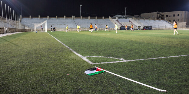 eine Gruppe Frauen trainiert auf einem Fußballplatz, vor ihnen liegt eine umgeworfene Eckfahne mit Palästina-Fähnchen