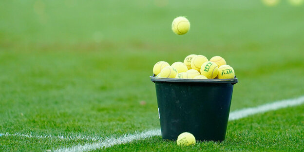 Ein Eimer mit Tennisbällen steht auf einem grünen Sportplatz
