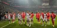 Spieler von FC Bayern in rot-weißen Trikots stehen am Rand des Spielfeldes, im Hintergrund die hohe Zuschauertribüne