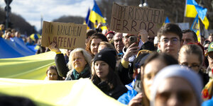 Demonstranten stehen mit ukrainischen Flaggen und Schilder wie "Wir brauchen Waffen" neben einer gigantischen ukrainsichen Flagge