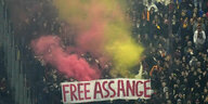 Eine Demo mit "Free Assange"-Banner, roter und gelber Rauch steigt auf
