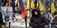 Eine Frau sitzt allein am Grab eines Angehörigen auf dem Friedhof, der mit ukrainischen Flaggen geschmückt ist