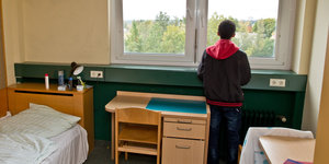Ein Junge steht im Zimmer seiner Flüchtlingsunterkunft und schaut aus dem Fenster