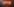 Künstler steht heruntergebeugt vor einer Liege, auf der eine Person liegt und tättowiert diese. Im Hintergrund sind rot leuchtende Leuchtkästen, auf denen Schriftzüge zu erkennen sind.
