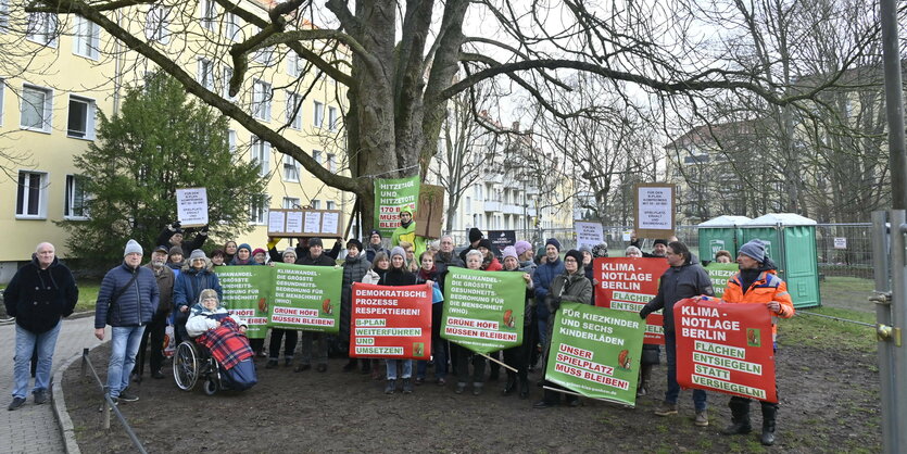 Menschen mit Plakaten stehen unter einem großen Baum