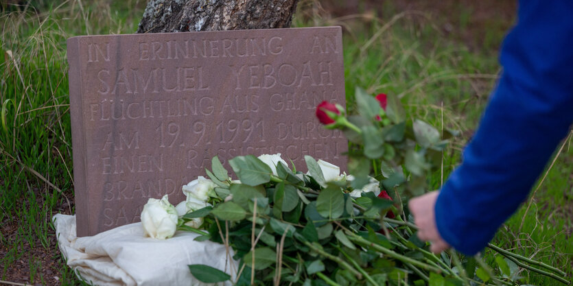 Eine Person legt an einem Gedenkstein eine Rose ab.