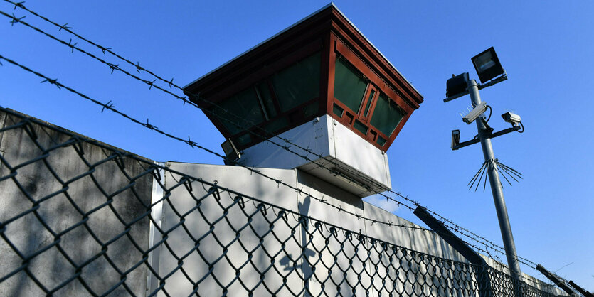 Wachturm, hohe Mauern und Scheinwerfer hinter Maschendraht und Stacheldrahtzaun