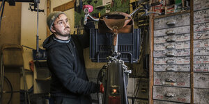 Ein junger Mann mit Mütze kniet und arbeite an einem Fahrrad in einer Werkstatt