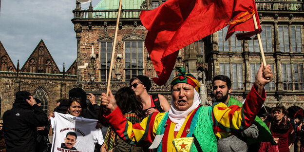 Eine Frau, gekleidet in die kurdischen Farben rot, gelb und grün, steht bei einer Demonstration auf dem Bremer Marktplatz.