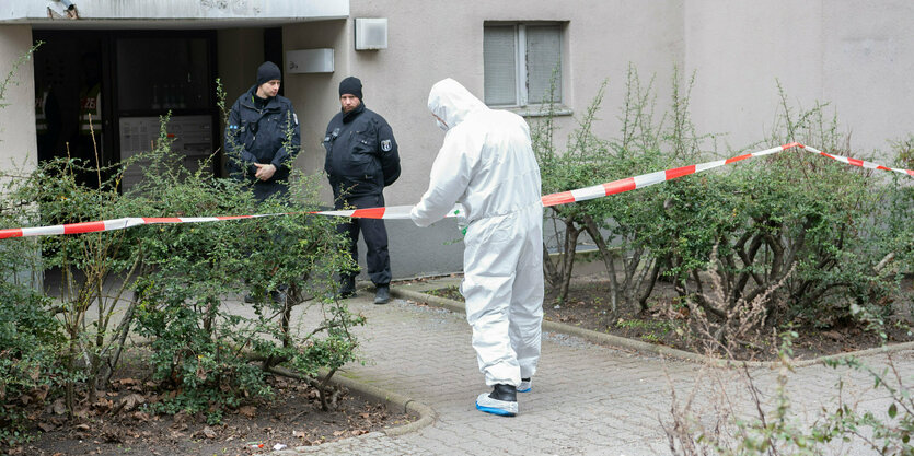 Berlin: Polizisten stehen am Eingang eines Mehrfamilienhauses in Stadtteil Kreuzberg, während ein Polizist in Schutzanzug an einem Absperrband steht