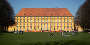 Studierende sonnen sich im Schloßgarten vor einem historischen Gebäude der Universität Osnabrück.