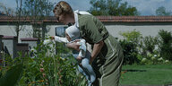 Eine Frau mit Baby beugt sich zu einem Blumenbeet herunter