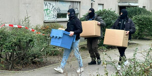 Vermummte Polizisten bringen Kartons aus einem Mietshaus