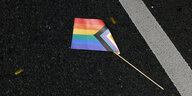 Eine Progressive Pride Flag liegt auf dem Boden einer Straße