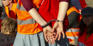 Handschellen halten Hände einer:s Aktivist:in auf dem Rücken fest