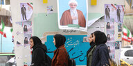 Drei junge Frauen mit Kopftüchern gehen an Wahlkampfplakaten für die Parlamentswahlen in Teheran vorbei