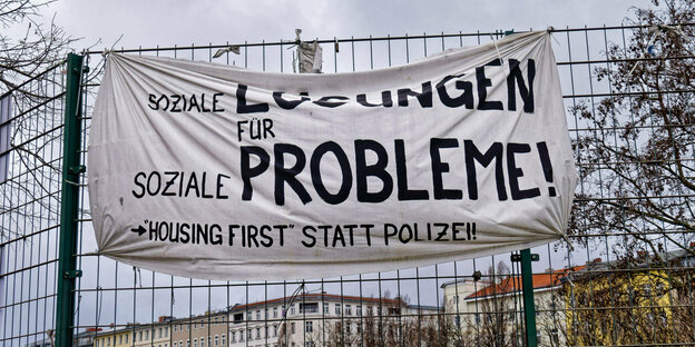 An einem Zaun hängt ein Banner auf dem steht: Housing first statt Polizei.