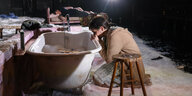 Schauspielerin kniet auf Theaterbühne im Schnee vor einer Badewanne