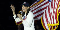 Nikki Haley im weißen Wollpullover mit Stars and Stripes auf der Brust, auch hinter ihr weht eine amerikanische Fahne im Wind